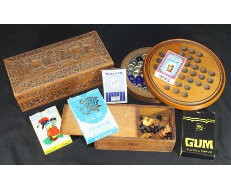 A turned wooden marble solitaire board with marbles, together with a miniature wooden carved chess set, five packs of playing