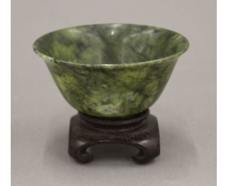 A Chinese green spinach jade bowl on wooden stand. 10 cm diameter.