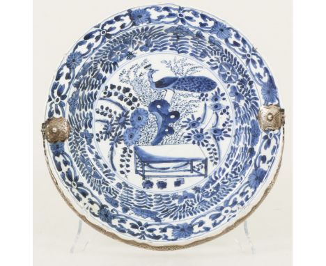   Een porseleinen bord met floraal decor, in het centrum gedecoreerd met o.a. een pauw. China, Kangxi. Zilveren heft, randsch