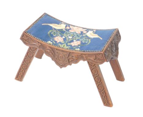 A Victorian oak stool, the curved seat with brass studded tapestry decorated with birds and flowers, floral and foliate carve