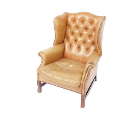 A Georgian style mahogany wing back club armchair, upholstered in button back tan leather, with loose cushion raised on flute