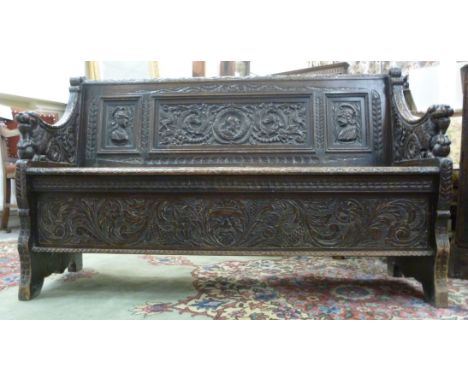 A mid/late 19thC profusely carved oak settle, having a level, low back, set with three portrait panels, between swept, enclos