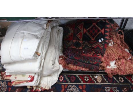 A shelf containing a quantity of curtains, tie-backs and an American blanket