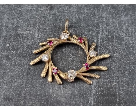 A yellow metal diamond and ruby swirl pendant, having textured surface, 34mm diameter. 