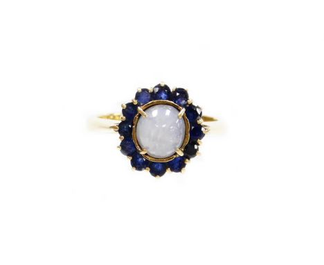 A moonstone and sapphire cluster ring, the central oval cut moonstone set in four claw setting with various sapphire surround