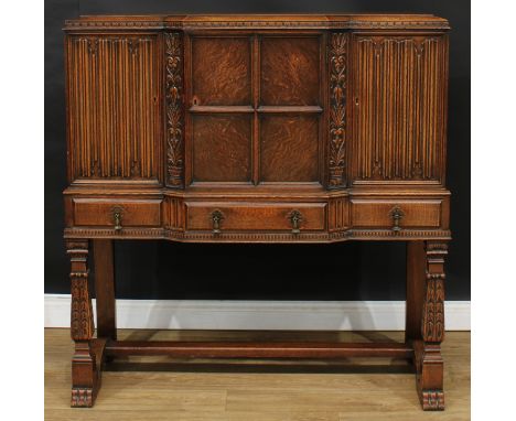 An oak side cabinet, central door flanked by linenfold doors, the left enclosing pipe provisions, above three drawers, 127cm 