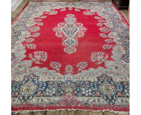 A Persian Kerman carpet, with a central floral motif on a red ground, with a floral border, 432 x 285cm.