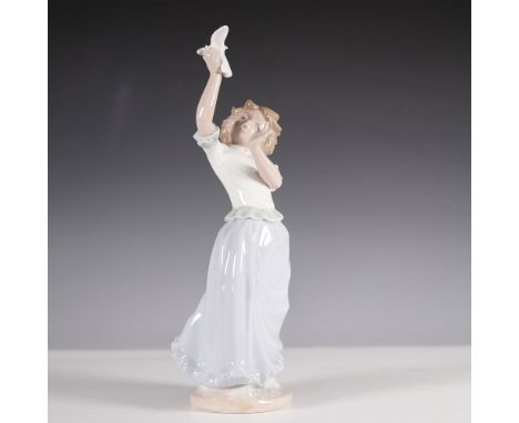 A charming Nao by Lladro porcelain figurine depicting a young girl joyfully holding a dove in the air. Designed with delicate