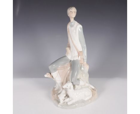A Nao by Lladro porcelain figurine depicting a young shepherd seated on a rock with three lambs at his feet. The figure is dr