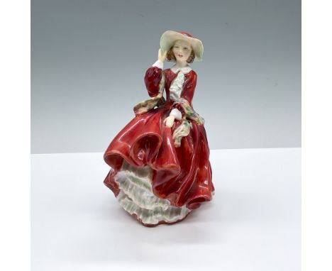 Hand decorated figure of a woman in a long red dress, red bonnet with a blue ribbon, and multicolored shawl. She is standing 