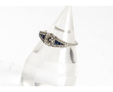 An Art Deco sapphire and diamond dress ring, the central cushion cut diamond flanked by pave set tapered sapphires surrounded