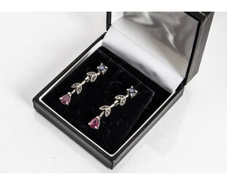 A pair of sapphire and ruby silver set drop earrings, the circular cut sapphires supporting marcasite set silver leaves termi