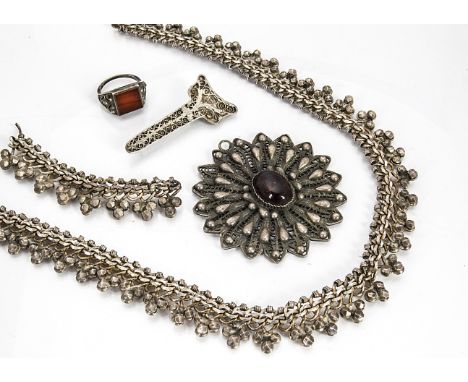 A collection of North African silver jewels, including a fringe necklace, a paste set filigree medallion, a carnelian gentlem