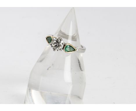 A three stone emerald and diamond dress ring, the central brilliant cut diamond in six claw setting flanked by pear cut emera