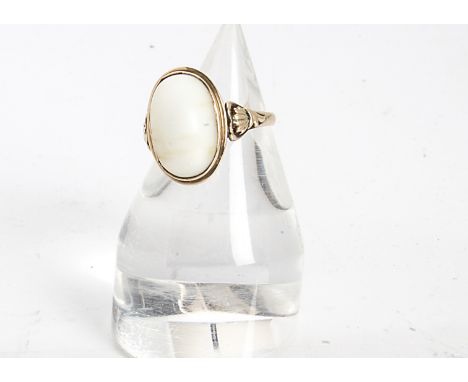 A white gem set cabochon ring, in yellow metal, the oval stone with chatoyant set in a rubbed over setting with ornate should