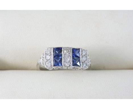 A SAPPHIRE AND DIAMOND RING set with four square-shaped sapphires and with graduated circular-cut diamonds, in 18ct. white go