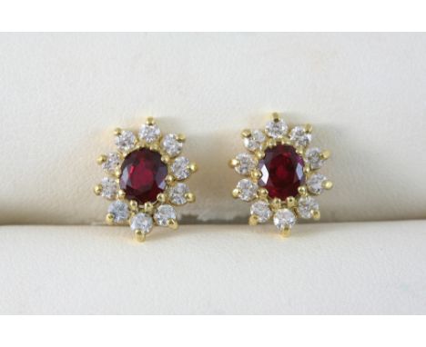 A PAIR OF RUBY AND DIAMOND CLUSTER STUD EARRINGS each set with an oval-shaped ruby within a surround of circular-cut diamonds