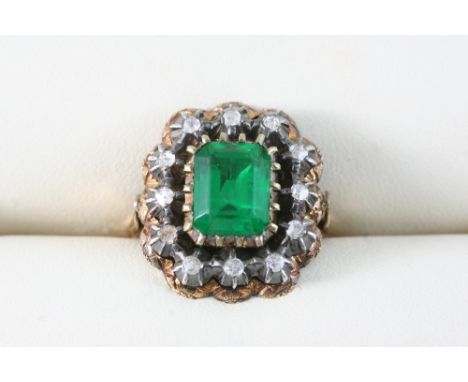 A PASTE SET AND GOLD RING centred with a rectangular-shaped green paste stone within a surround of circular white stones, in 