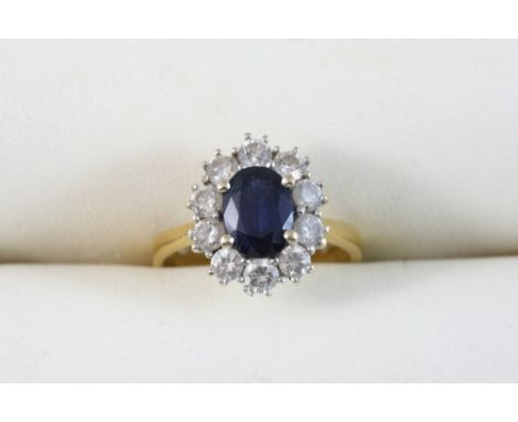 A SAPPHIRE AND DIAMOND CLUSTER RING the oval-shaped sapphire is set within a surround of circular-cut diamonds, in gold. Size