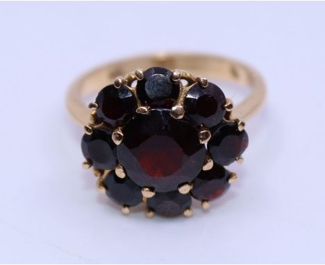 A precious yellow metal and garnet dress ring, the domed head claw set central round cut garnet bordered by ring of eight fur