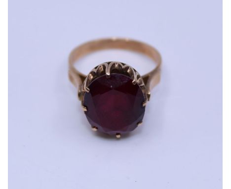 A precious yellow metal and synthetic ruby ring, claw set large central oval mixed cut synthetic ruby, (yellow metal assessed