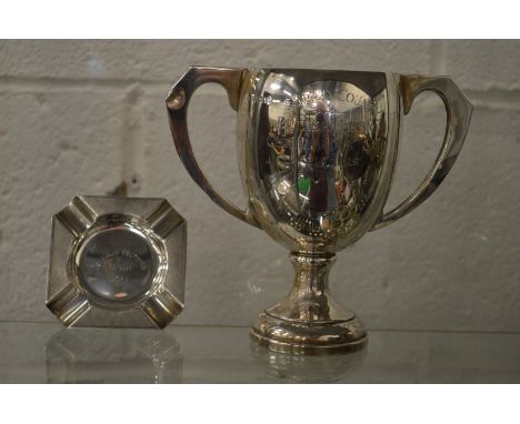 A silver twin handled trophy cup and an ashtray.