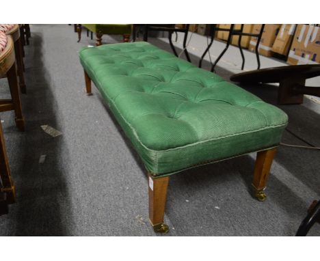 A button upholstered long footstool on tapering legs with brass castors.