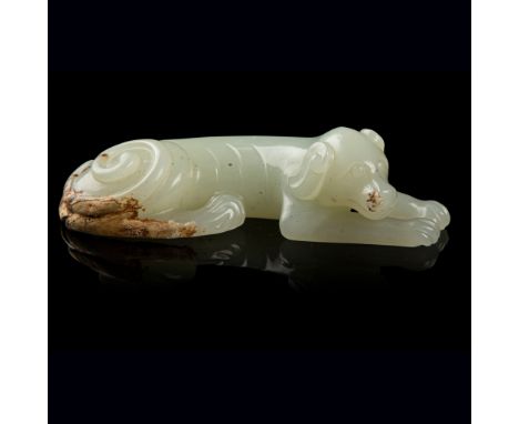 PALE CELADON JADE DOG carved as a slender recumbent dog with its head slightly raised to right above two front legs, ears tuc