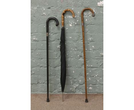 An ebonized walking stick with silver collar, similar stepped bamboo example and an umbrella.