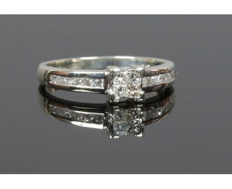 A 9ct white gold ring set with four square cut diamonds and with channel set diamond shoulders, size L.