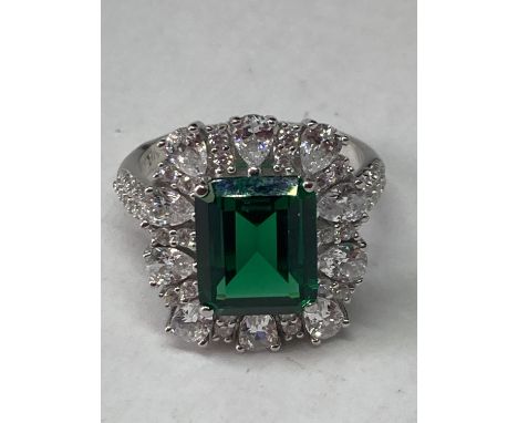 A WHITE METAL RING WITH A LARGE RCTANGULAR LABORATORY EMERALD SURROUNDED BY CLEAR STONES ALSO ON THE SHOULDERS SIZE P 