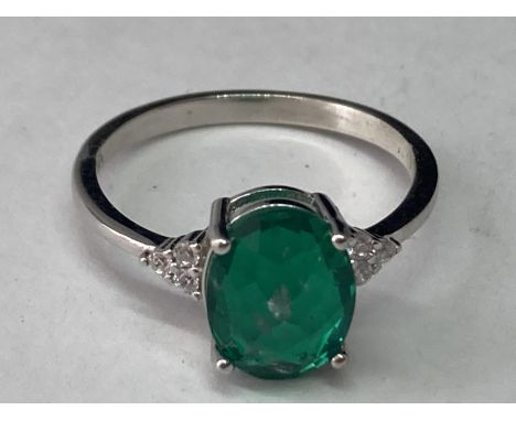 A WHITE METAL RING WITH AN OVAL LABORATORY EMERALD WITH THREE CLEAR STONES TO EACH SIDE SIZE Q/R 