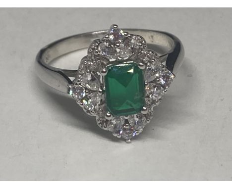 A WHITE METAL RING WITH A RECTANGULAR  LABORATORY EMERALD SURROUNDED BY CLEAR STONES SIZE Q/R 