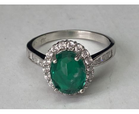 A WHITE METAL RING WITH A CENTRE LABORATORY GROWN EMERALD WITH CLEAR STONES SURROUNDING AND ON THE SHOULDERS SIZE Q/R 