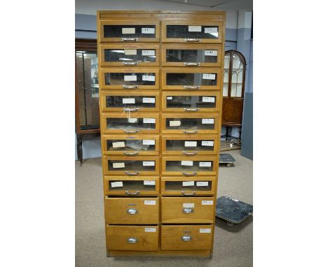 A vintage light oak haberdashers cabinet fitted with sixteen glass-fronted drawers above four further drawers and with two sp