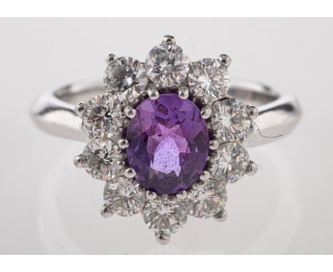 A platinum, purple sapphire and diamond ring, the central oval cut purple sapphire claw set within a surround of brilliant cu