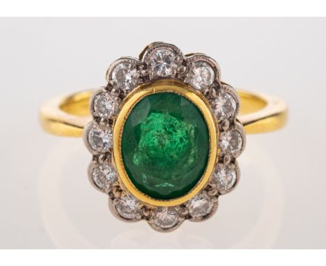 An emerald and diamond ring, the central oval cut emerald collet set within a surround of brilliant cut diamonds, stamped 750