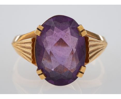 A dress ring set with an oval faceted amethyst, the shoulders cut with fan form grooves, marked 750 for 18ct gold, amethyst 1