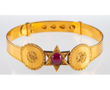 A gold bangle with a cabochon ruby in star setting bordered by floral engraved decoration, ruby 7.2 x 6.5 mm, marked  22ct go