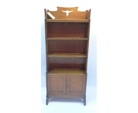 An Arts and Crafts oak waterfall bookcase with four shelves above two cupboard doors and raised on carved bracket feet, H 135