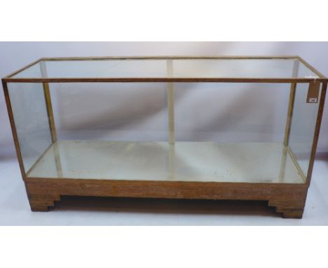 An Art Deco oak framed and glass shop display case,  with mirrored bottom and raised on carved bracket feet, H 92 x W 178 x D