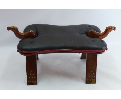 A teak saddle stool in the form of a camel with red and black leather seat, H 44 x W 84 x D 34cm 