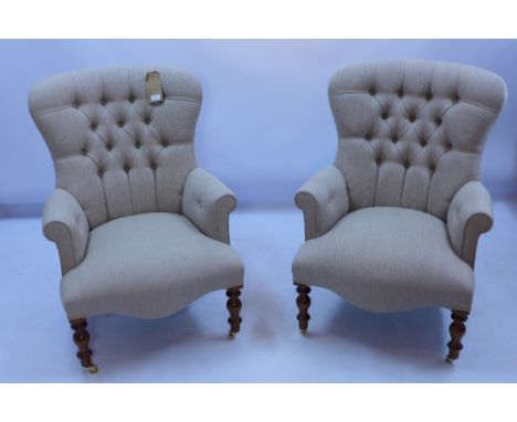 A pair of button back armchairs upholstered in stone linen, raised on turned legs and castors