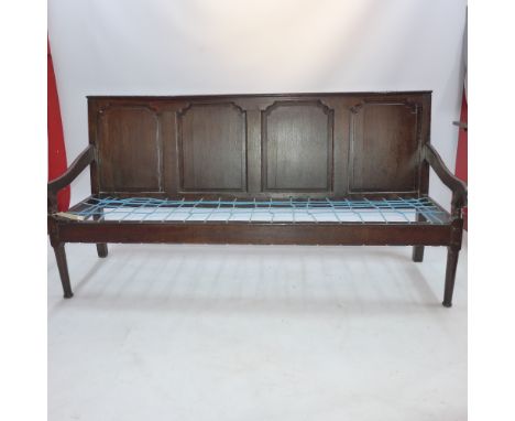 A late 18th / early 19th century oak settee with four panelled back, scroll arms and raised on circular tapered legs (lacking