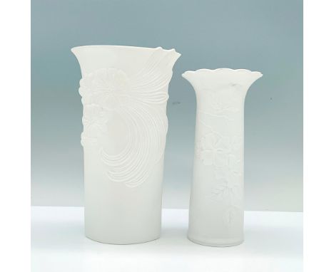 A pair of white porcelain vases that have high relief patterns of floral designs on them both, one being circular in shape an