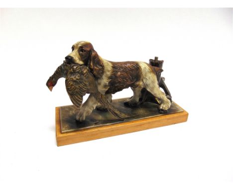 AN AUSTRIAN CAST AND PAINTED TABLE LIGHTER in the form of a spaniel holding a pheasant in its mouth by a tree trunk, on a rec