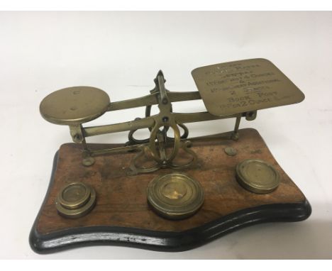 A set of early 20th century brass postal scales with weights on a walnut plinth.