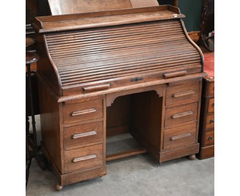 An early 20th century oak roll-top desk with sliding tambour panel enclosing fitted interior over six drawers, 120 x 60 x 120