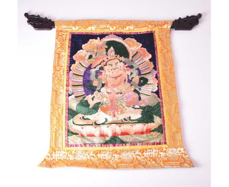 A Tibetan embroidered thangka of the god JambhalaMid-20th century, with carved hardwood support, 70cm x 61cm, together with a