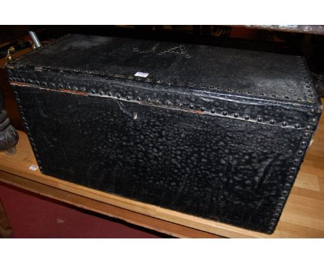 A leather clad and studded hinged top travelling trunk, having end carry handles, the cover monogrammed JA, w.83cm
